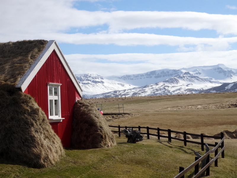 Vue d'une ferme islandaise à la façade rouge sur fond de montagnes enneigées
